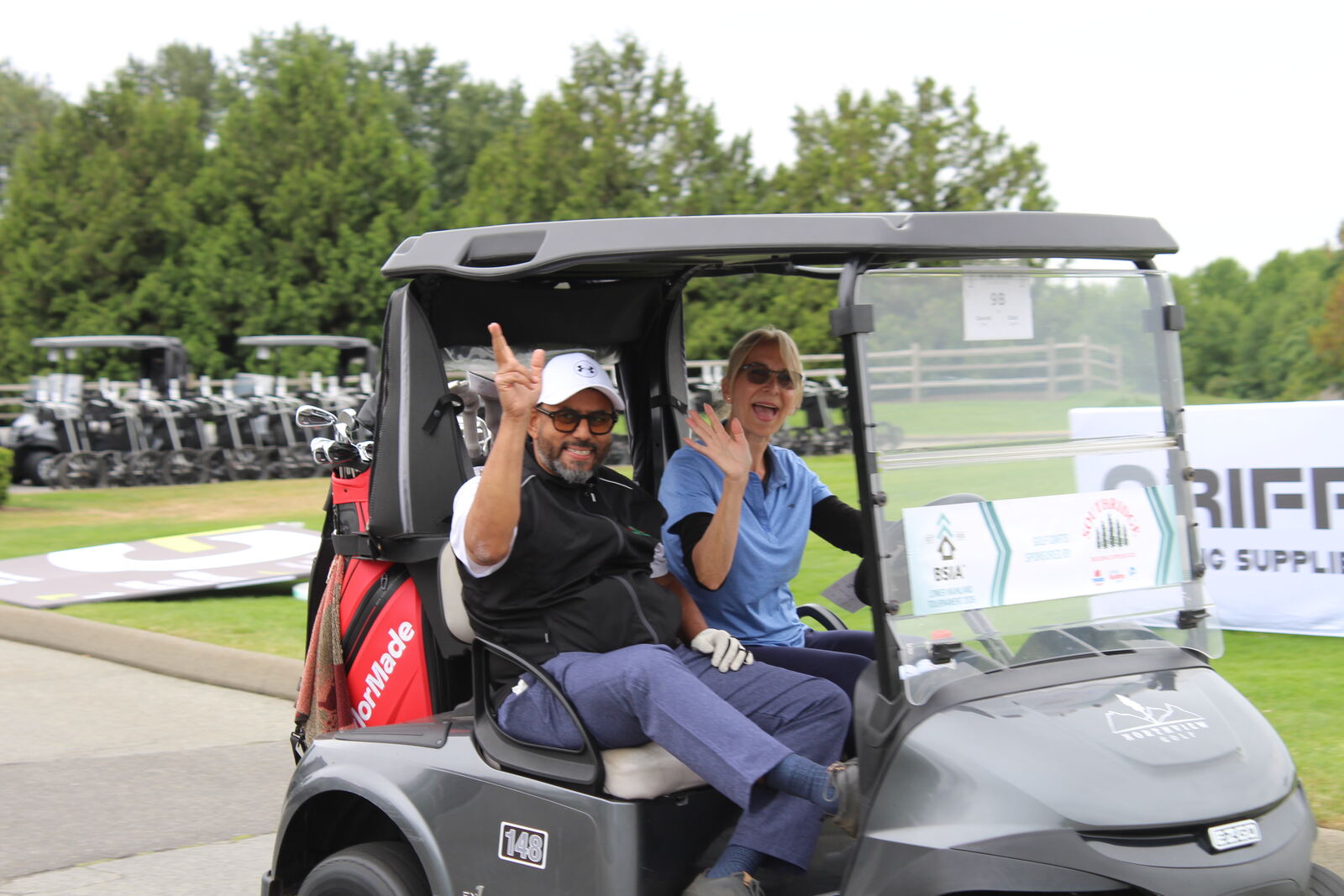 Two golfers waving from their cart on the way out