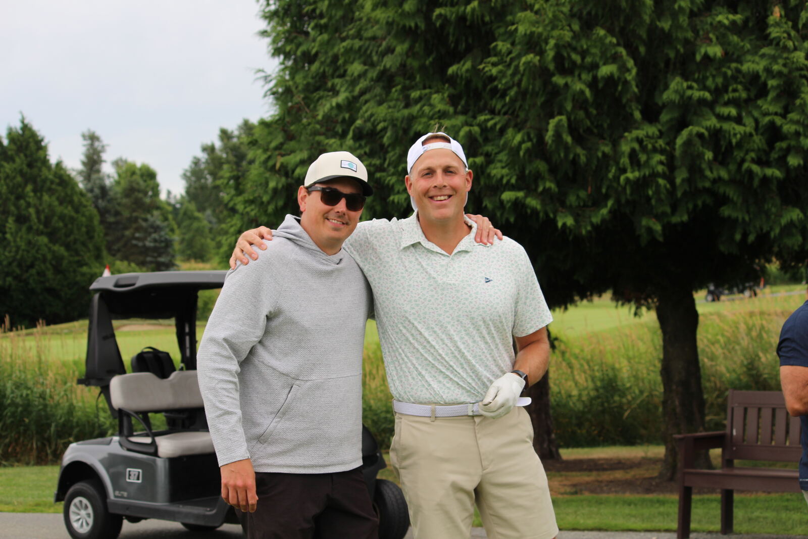 Two golfers posing together beside a cart