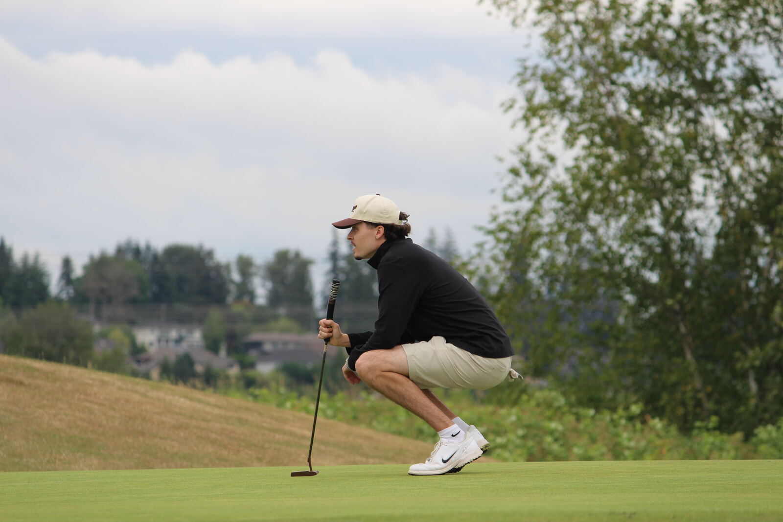 A golfer crouching to read the line of his putt